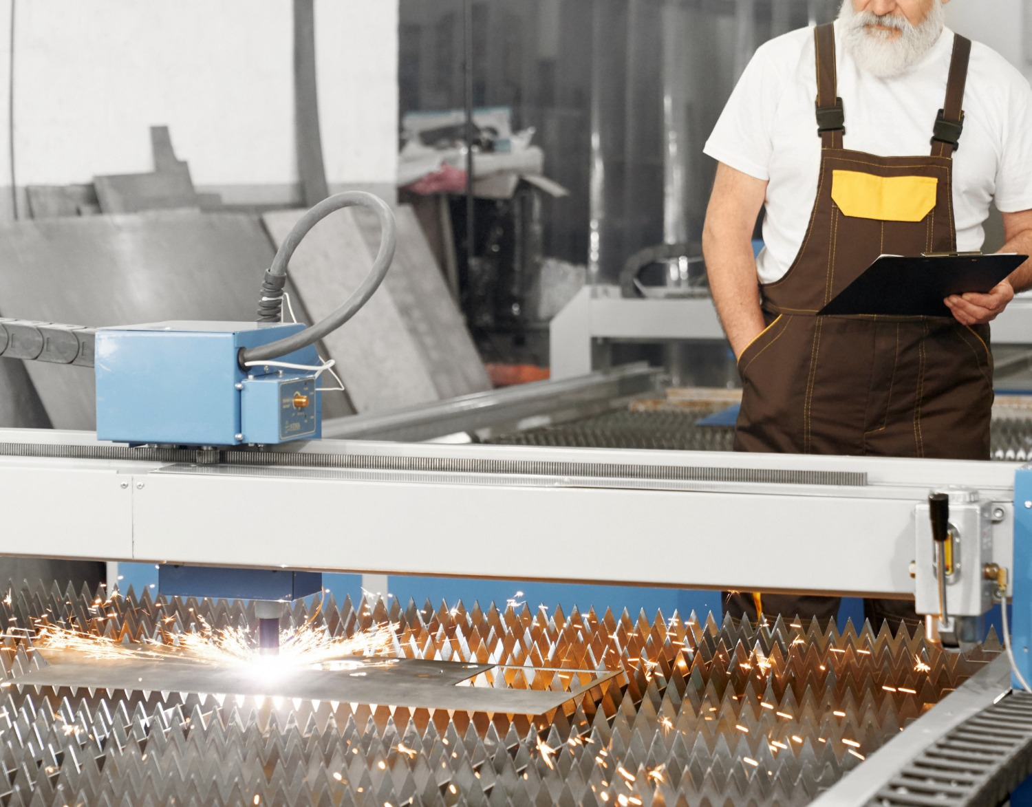 Factory worker supervising a CNC laser metal cutting machine operation in a manufacturing plant